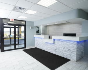 Guest check-in desk, large floor mat, two sets of double doors leading to hotel exterior, tiled flooring