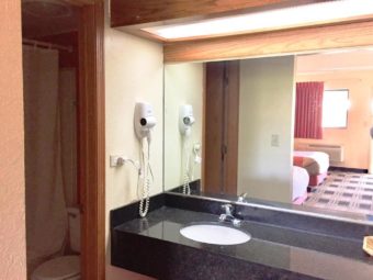 Vanity unit with sink, wall mounted hair dryer, wall mounted mirror, overhead strip light, doorway to shower tub and toilet
