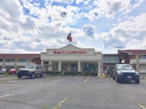 hotel entrance with canopy, small bushes, american flag, two story buildings, parking spaces