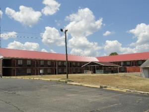 Two storey hotel building in an L shape, BBQ pavillion and grassy areas, walkways and parking area