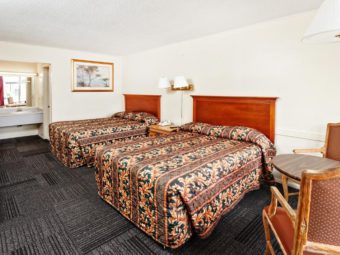 Two double beds, small table with two chairs, ceiling light, wall mounted bedside lights, night stand with telephone, wall mounted art, fridge, carpet flooring and alcove with vanity unit and large wall mounted mirror with overhead strip light