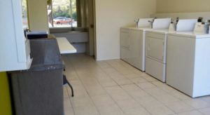 Guest laundry with coim operated washing machines and dryers, table, tiled floor and alcove with vanity unit and large wall mounted mirror