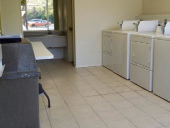 Guest laundry with coim operated washing machines and dryers, table, tiled floor and alcove with vanity unit and large wall mounted mirror