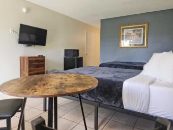 Two double beds, art image, table and chair, wooden drawer unit, wall mounted TV, fridge with microwave, tiled flooring