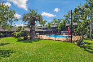 Outdoor pool with fenced surround, grassy area with trees,