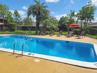 outdoor pool with fencing, patio tables with umbrella and chairs, sun loungers