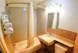 Shower tub with shower curtain, sink, wall mounted mirror with overhead lights, toilet, wall mounted towel rack with towels