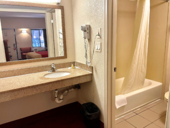 Vanity unit, mirror, hairdryer, doorway to bathroom, showertub with shower curtain, tiled flooring