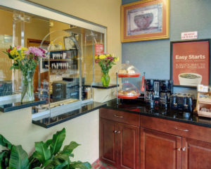 Guest check in desk, flowers in vases, art image, breakfast display counter with breakfast pastries, coffee pots and toaster