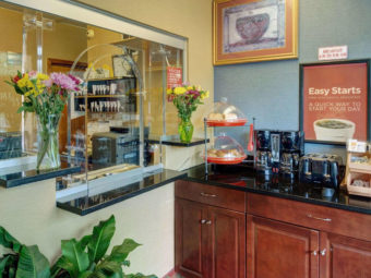 Guest check in desk, flowers in vases, art image, breakfast display counter with breakfast pastries, coffee pots and toaster
