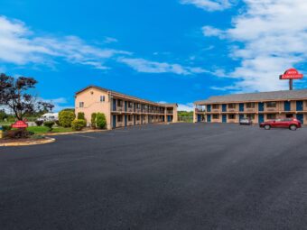 Two two story buildings with covered walkways, stairways and exterior guest room entrances, landscaping with grassy area, small trees and shrubs, parking spaces