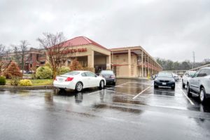 Hotel entrance, two story hotel building, parking spaces, landscaped area with small trees and bushes