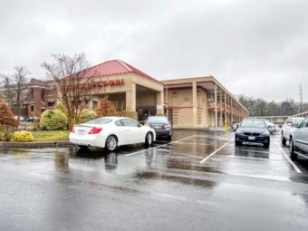 Hotel entrance, two story hotel building, parking spaces, landscaped area with small trees and bushes