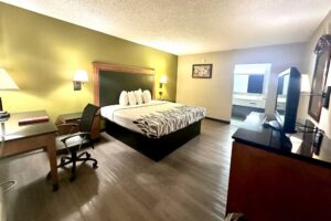King bed, night stands, bedside lights, desk with lamp and chair, unit with TV, mirror, laminate flooring, alcove with vanity unit, mirror, tiled flooring