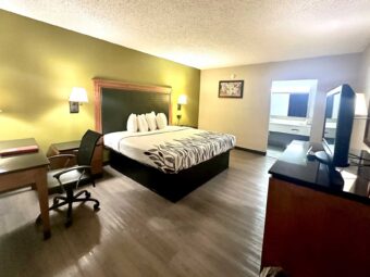 King bed, night stands, bedside lights, desk with lamp and chair, unit with TV, mirror, laminate flooring, alcove with vanity unit, mirror, tiled flooring