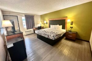 king bed, night stands with clock, wall bedside lights, desk with lamp and chair, fridge, unit with TV, wall light, laminate flooring