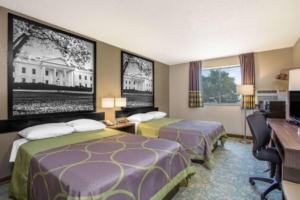 Two queen beds, night stand with bedside lamp, telephone and clock, floor lamp, fridge with microwave, hanging shelf, desk with TV and office chair, carpet flooring