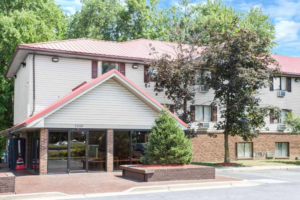 Hotel entrance, two story building, landscaping with trees and parking spaces