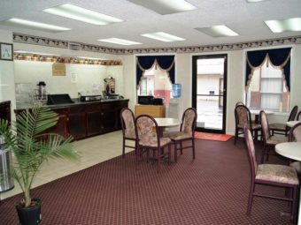 Tables and chairs, welcome mat, breakfast display counter, microwave, toaster, water dispenser, potted plant and carpet flooring