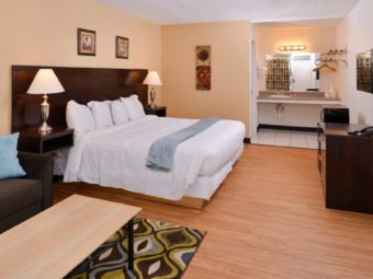 Sofa, coffee table, king bed, night stands with bedside lamps, wall mounted art, vanity unit with sink, bathroom amenities, ice bucket, disposable cups, wall mounted towel rack with towels, large wall mounted mirror with overhead lighting, metal hanging rail with hangers and overhead shelf, fridge, microwave, wooden unit with storage drawers and telephone, wall mounted flat screen tv, rug and laminate flooring