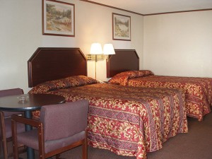 Two double beds, night stand, wall mounted bedside lights, wall mounted art, small table and two chairs, carpet flooring