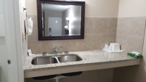 Vanity unit with double sink, wall mounted mirror, wall mounted towel ring with towels, ice bucket, tissues and bathroom amenities