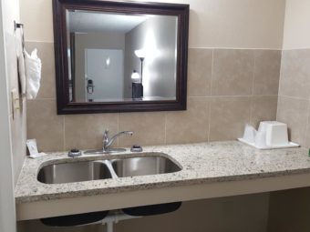 Vanity unit with double sink, wall mounted mirror, wall mounted towel ring with towels, ice bucket, tissues and bathroom amenities