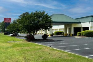 Hotel entrance with drive through canopy, parking spaces, brand signage, small trees, shrubs and grassy areas