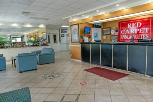 Guest check in desk, easy chairs, occasional table, mirrored wall behind shel with guest inforamtion and potted plants, tiled flooring with mat