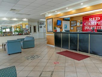 Guest check in desk, easy chairs, occasional table, mirrored wall behind shel with guest inforamtion and potted plants, tiled flooring with mat