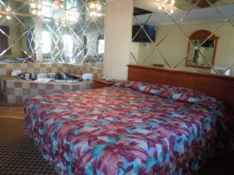 king bed, mirror head board, jacuzzi with bath mat, bathroom amenties, towels and mirrored walls