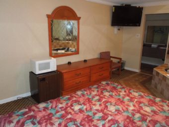 King bed, fridge, microwave, wall mounted mirror, wooden drawer unit, wall mounted tv, chair, carpet flooring, alcove with vanity unit and large wall mounted mirror
