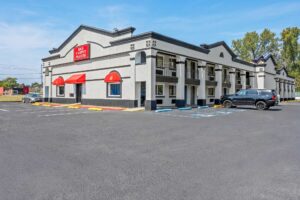 Two story building with exterior guest room entrances and walkways, parking spaces, grassy area and trees