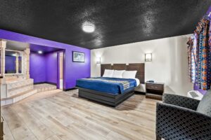 King bed, night stands with telephone, wall bedside lights, art image, easy chair, spa tub on raised tiled platform, doorway to bathroom, laminate flooring