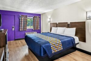 King bed, wall bedside lights, night stand, wooden unit with TV, laminate flooring