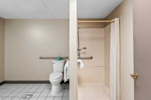 Walk in shower with greab handles and shower curtain, toilet, grab handle, towel rail with towels, tiled flooring