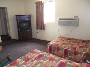 Two double beds, wooden tv console with tv, door way and two steps to bathroom, carpet flooring