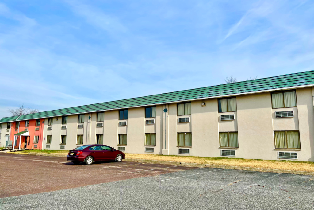 Two story building, hotel entrance with porch, parking spaces, grassy areas