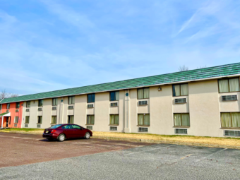 Two story building, hotel entrance with porch, parking spaces, grassy areas