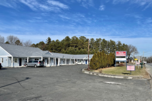 Hotel entrance, one story building, parking spaces,, brand signage on grassy area with small trees