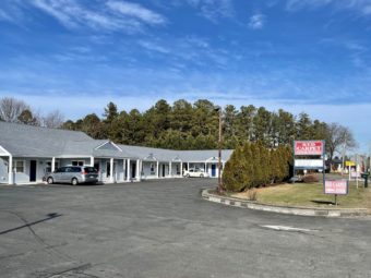 Hotel entrance, one story building, parking spaces,, brand signage on grassy area with small trees