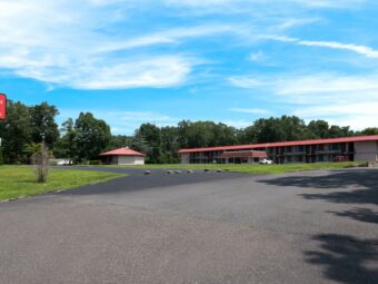 Brand signage, hotel entrance driveway, two story building with exterior guest room entrances, large grassy areas