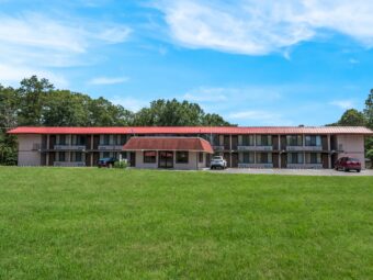 Two story building with covered walkways, stairways and exterior guest room entrances, hotel entrance, parking spaces, large grassy area