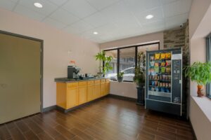 Counter with coffe machine, vening machine with snacks, plants in tubs, tiled flooring
