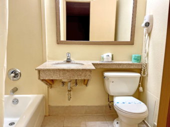 Shower tub, vanity unit, mirror, hairdryer, toilet, tiled flooring