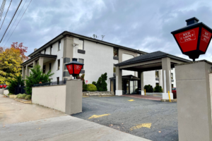 Hotel entrance with branded gate lamps, three story building, drive through canopy, parking area, landscaping with bushes andsmall trees