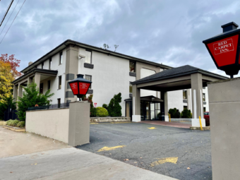 Hotel entrance with branded gate lamps, three story building, drive through canopy, parking area, landscaping with bushes andsmall trees