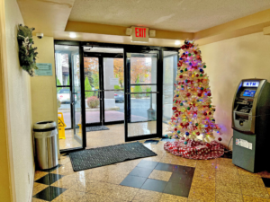Double entrance doors, decorated christmas tree, ATM machine, trash bin, tiled flooring with mats