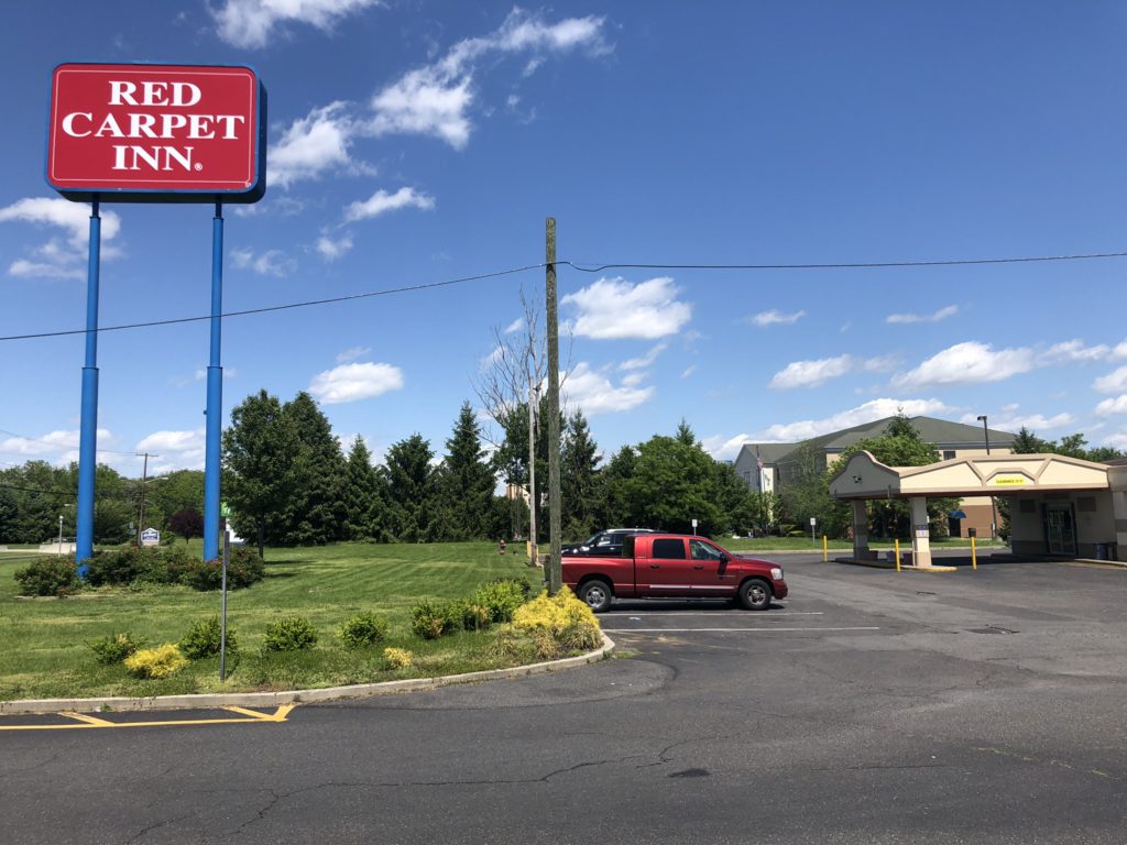 Hotel brand signage, grassy area with small bushes, hotel entrance canopy, parking spaces