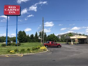 Hotel brand signage, grassy area with small bushes, hotel entrance canopy, parking spaces